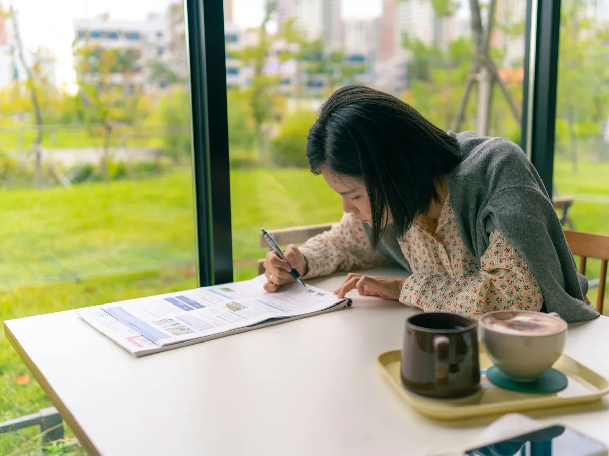 A young woman writing in a notebook by a sunny window